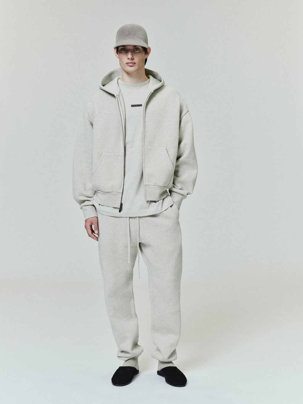 male model wearing light beige classic fleece zip-up hoodie with matching sweatpants and black slip-on shoes