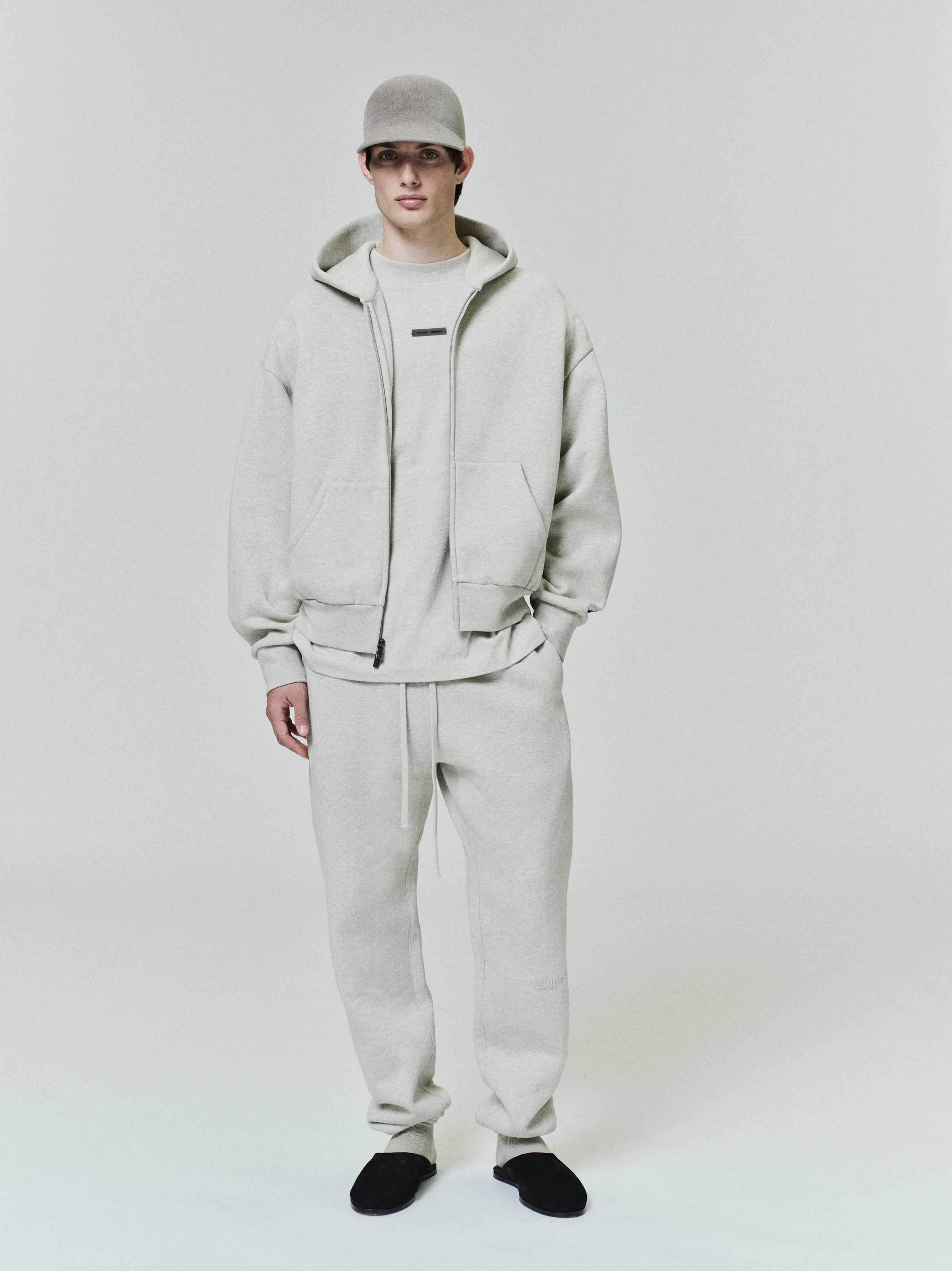 male model wearing light beige classic fleece zip-up hoodie with matching sweatpants and black slip-on shoes