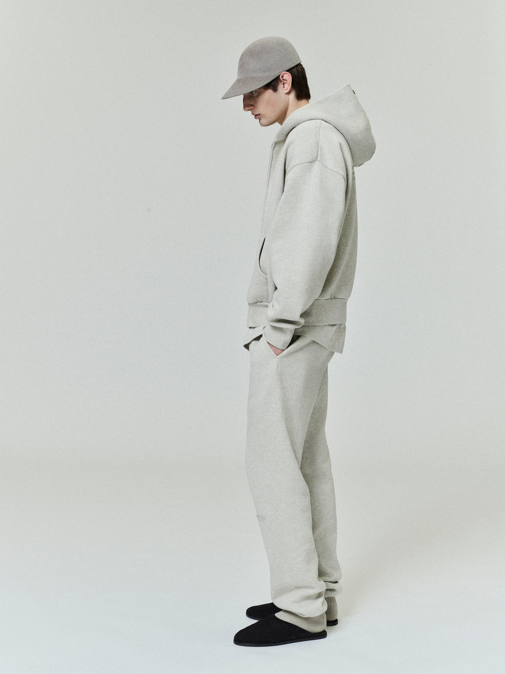 male model wearing light grey relaxed fit fleece zip-up hoodie with matching sweatpants and grey cap