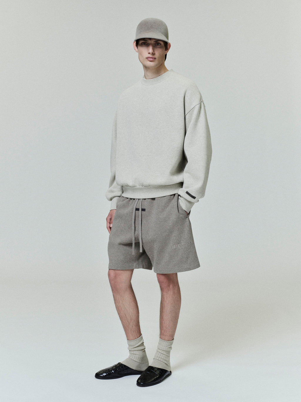 male model wearing relaxed fit heather gray fleece sweatshorts with elastic waist and drawstrings styled with matching sweatshirt and cap