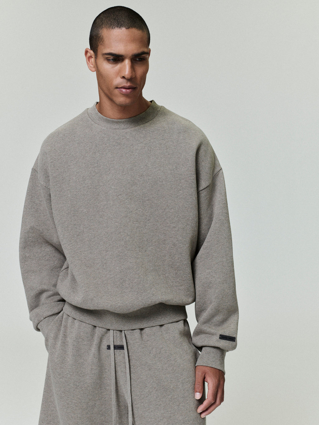 male model wearing oversized muted grey fleece crewneck with ribbed cuffs and relaxed fit against plain background