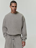 male model wearing oversized muted grey fleece crewneck with ribbed cuffs and relaxed fit against plain background