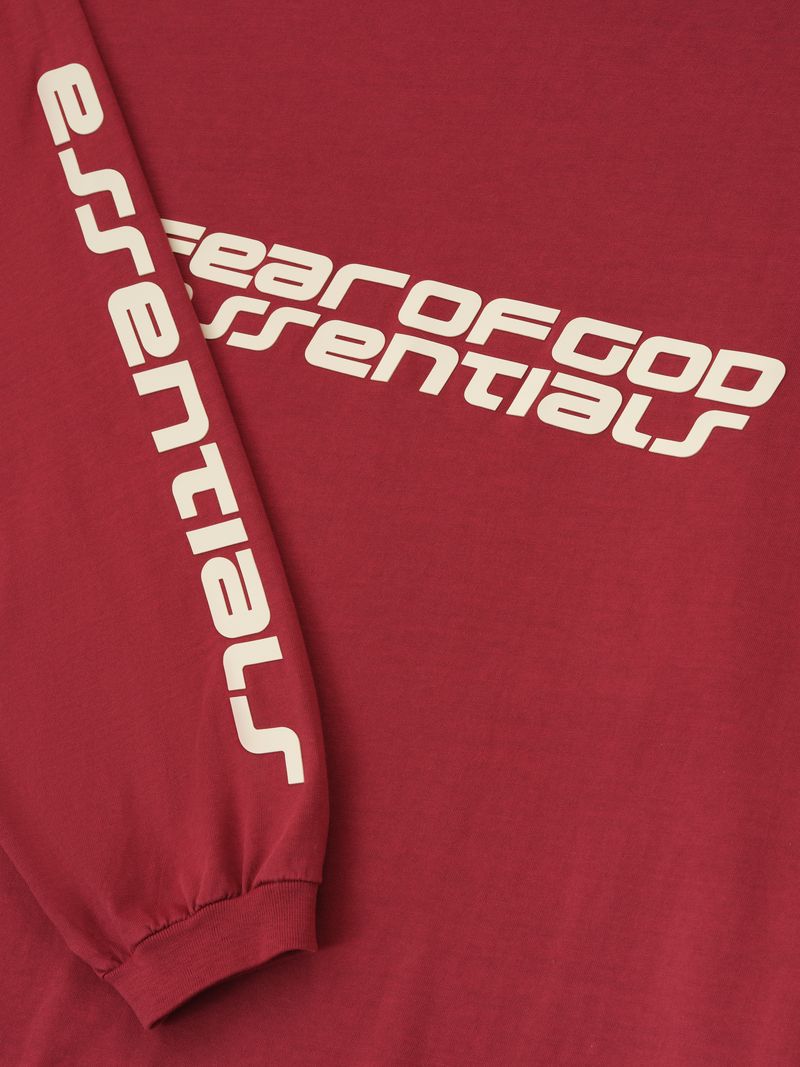 Close-up of crimson 90s Long Sleeve Tee showing angled Fear of God Essentials logo across chest and text on sleeve, gallery 0 Qjh_62VA.jpg