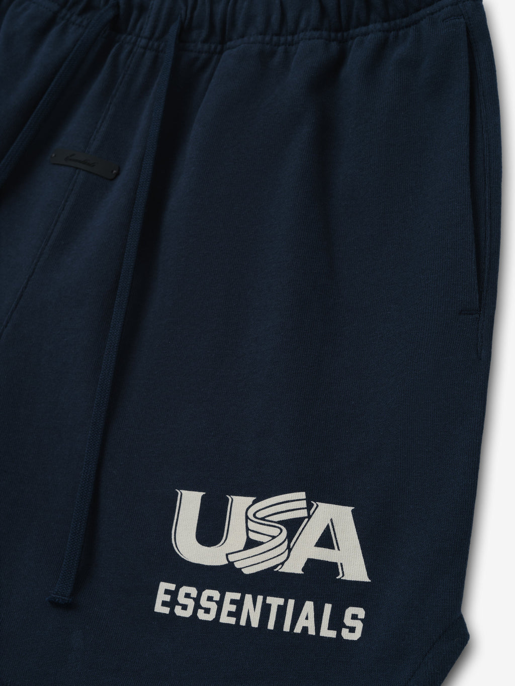Close-up of dark navy sweatpants with elastic waistband, drawstring, side pocket, and white "USA ESSENTIALS" graphic on leg