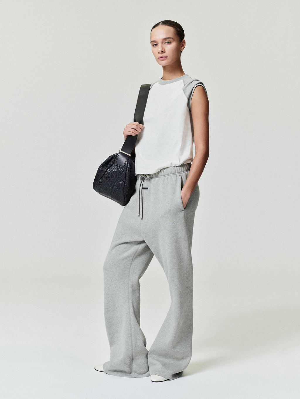 woman wearing light gray relaxed fit flare sweatpants with elastic waistband and sleeveless white top carrying black bag