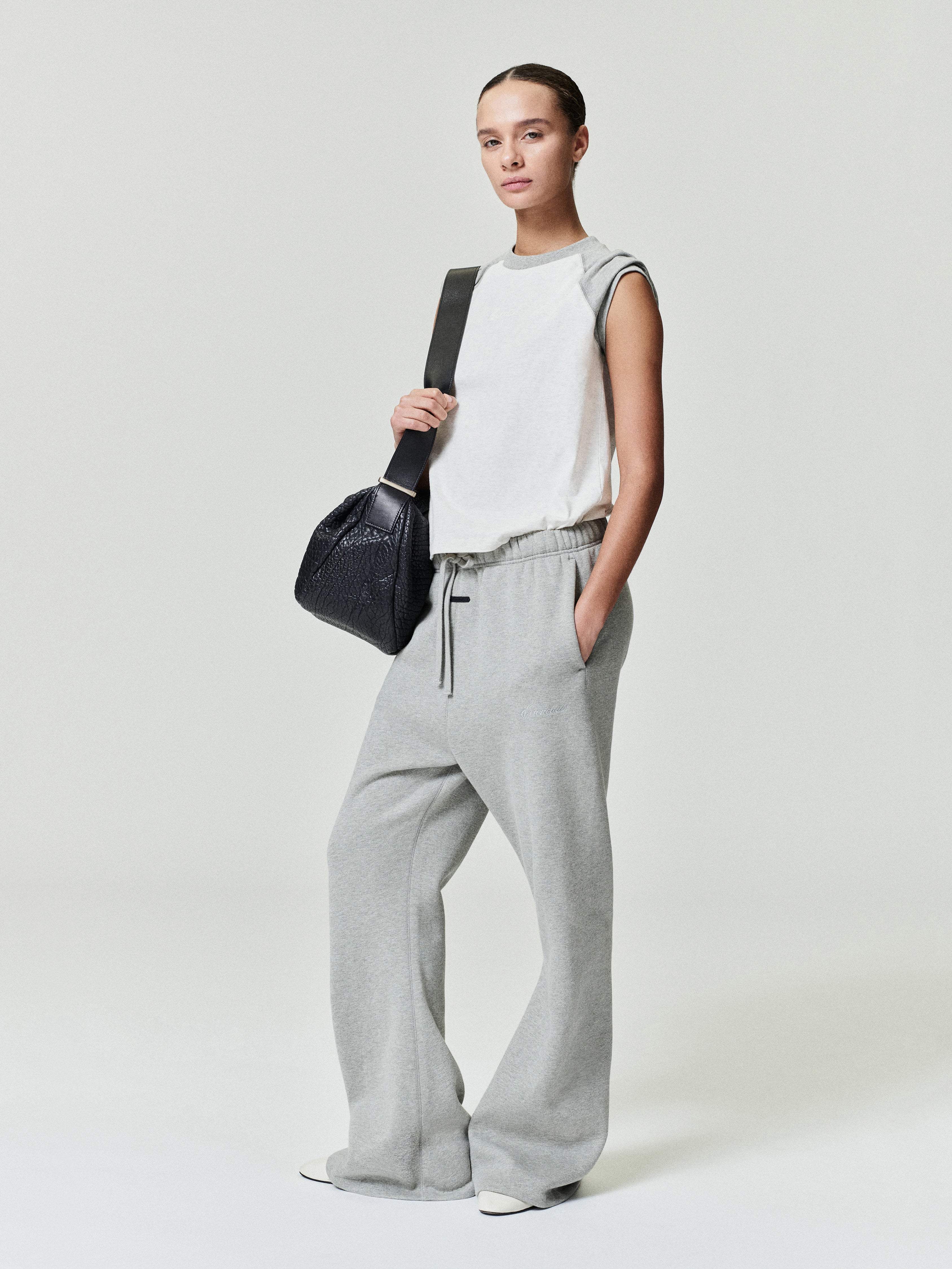 woman wearing light gray relaxed fit flare sweatpants with elastic waistband and sleeveless white top carrying black bag