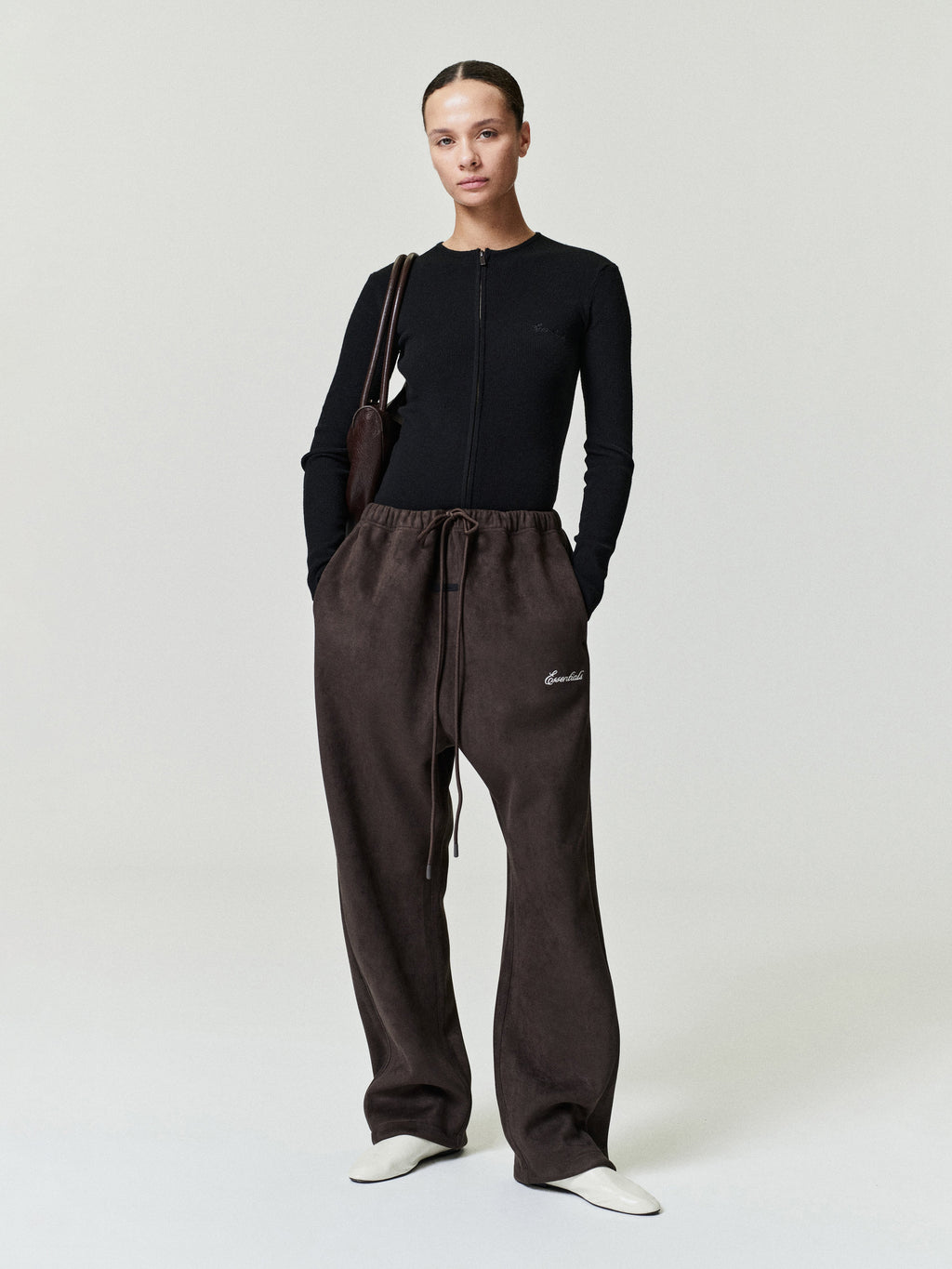 Person wearing a black top and brown pants with a visible brand logo on a white background