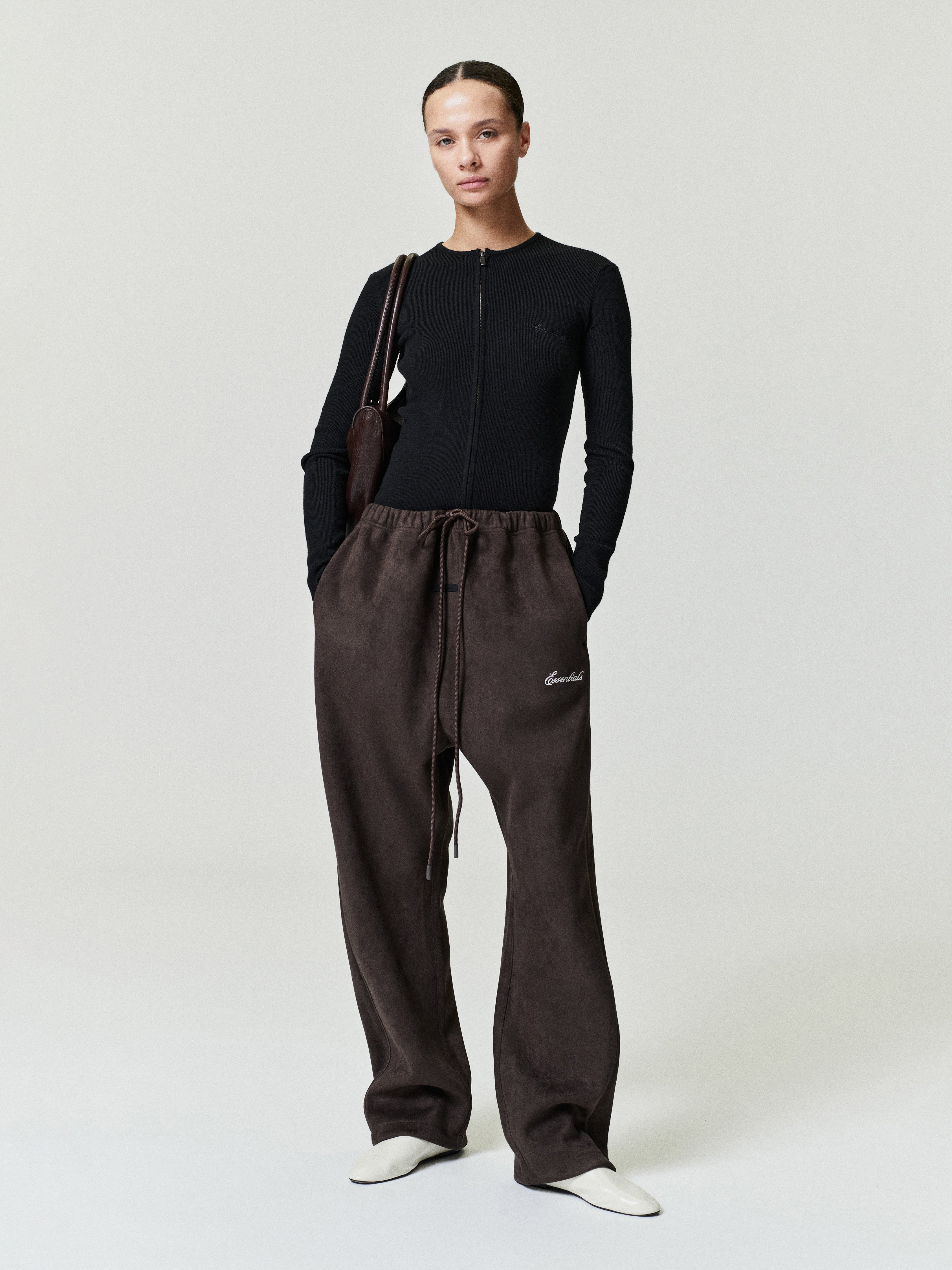 Person wearing a black top and brown pants with a visible brand logo on a white background