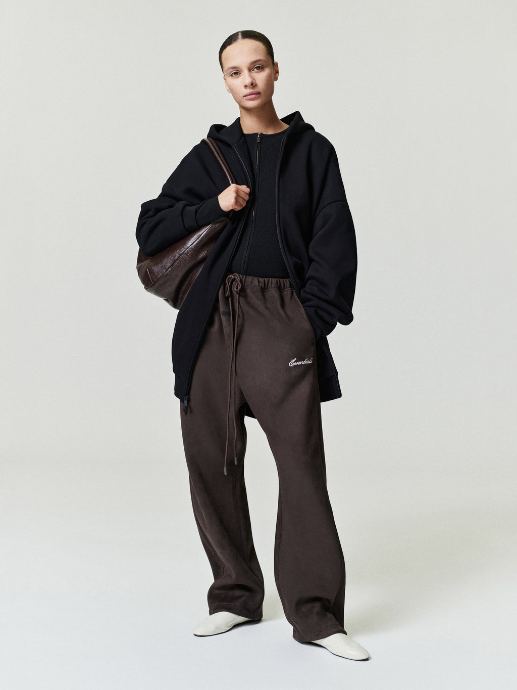 Person wearing a black hoodie and brown pants with a brown bag on a white background