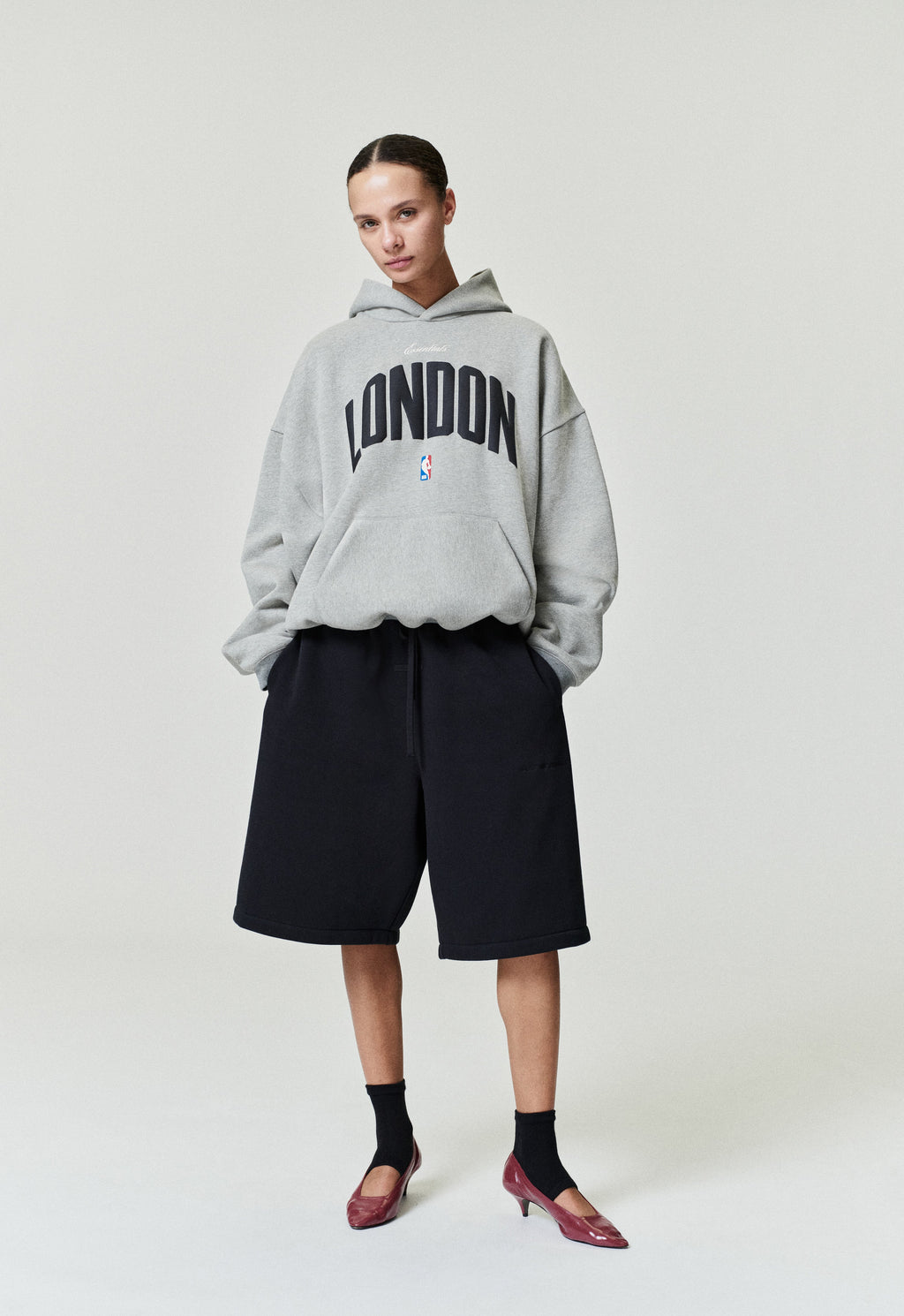 Model wearing grey London 90s Hoodie with black London text and small NBA logo, standing pose SP26_FW_L61-P_2895