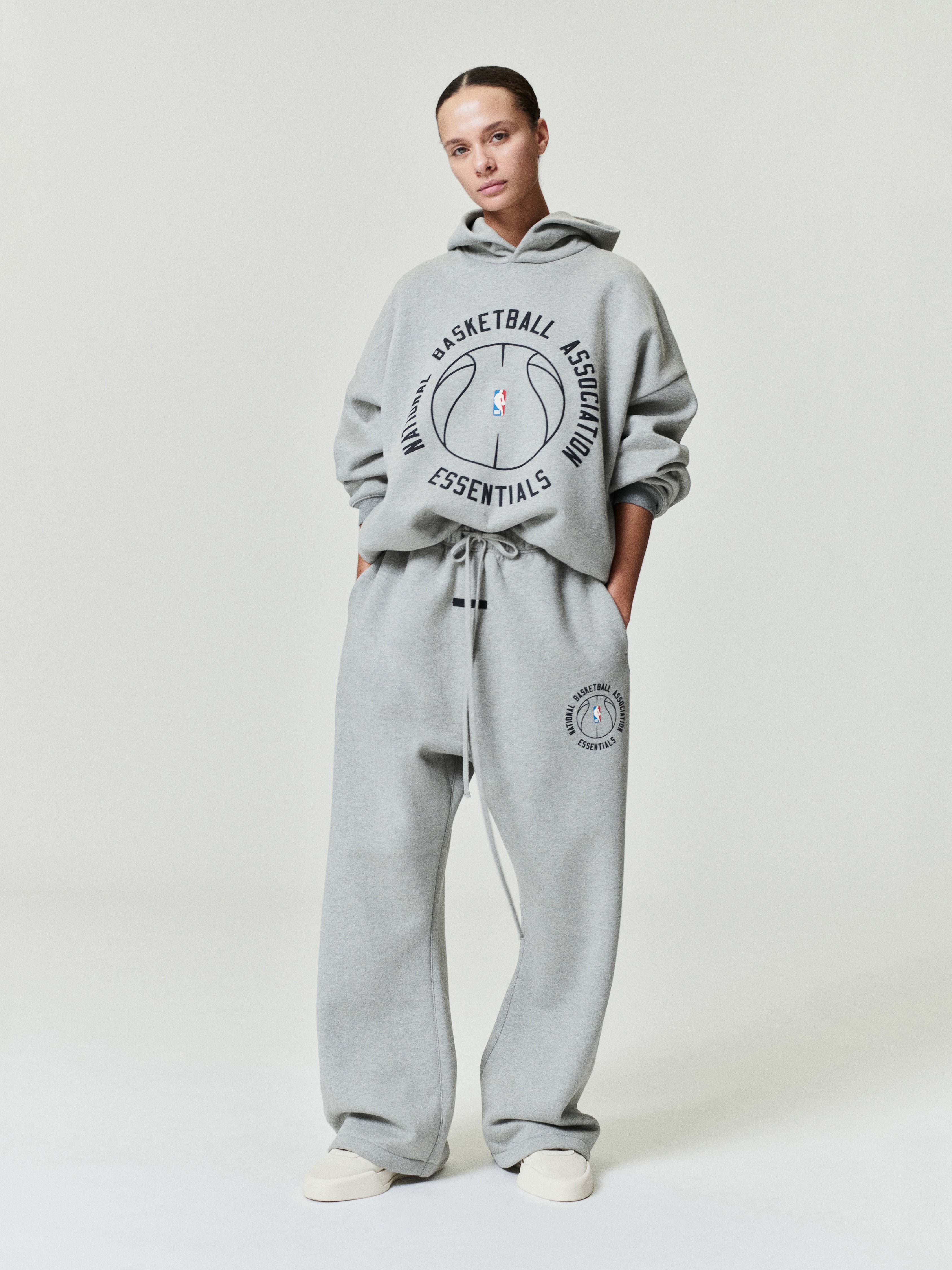 model wearing light gray heavyweight cotton fleece flare sweatpants with NBA Essentials circular logo and drawstring waist