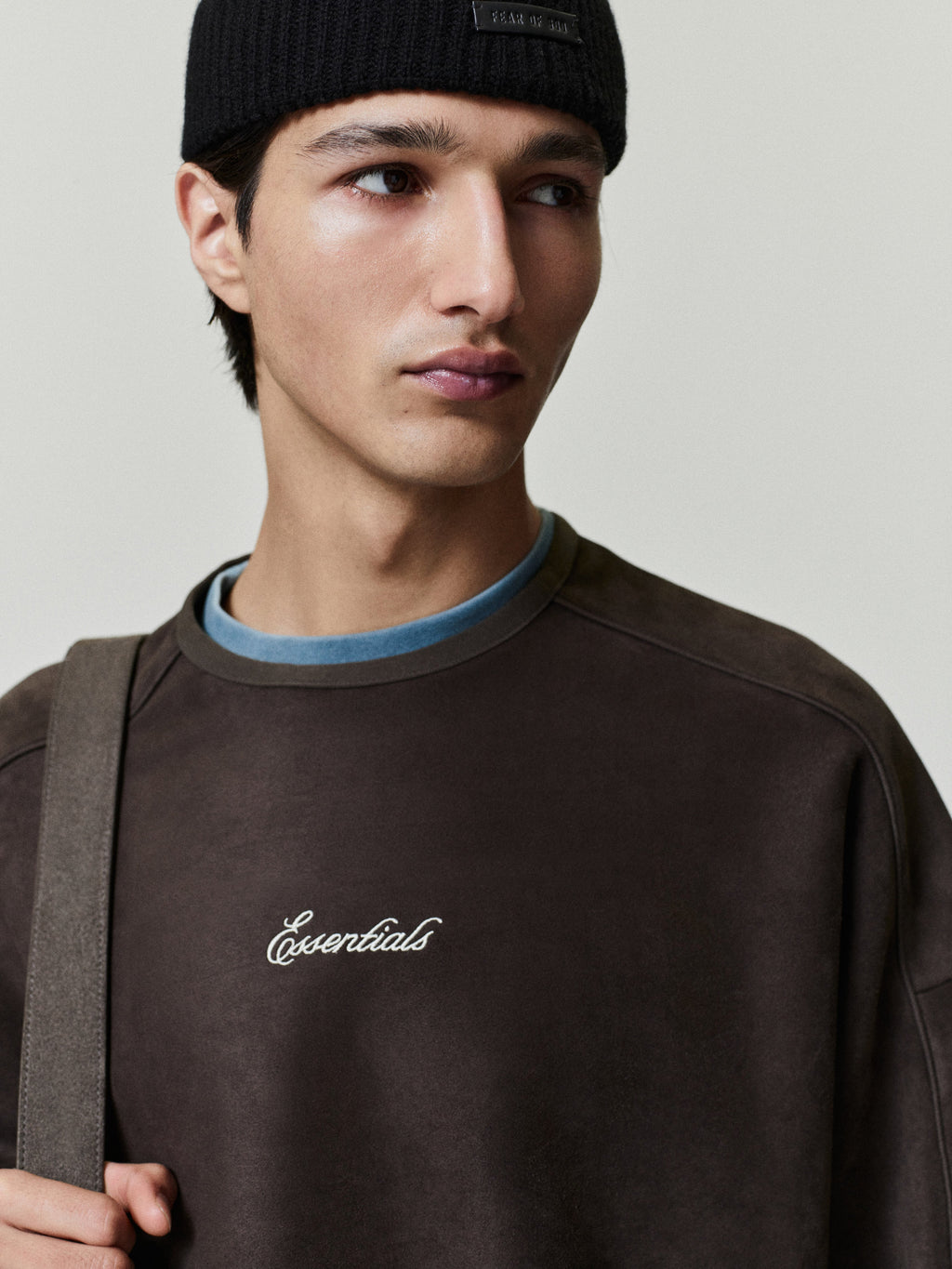 Person wearing a dark brown sweatshirt with 'Essentials' script logo