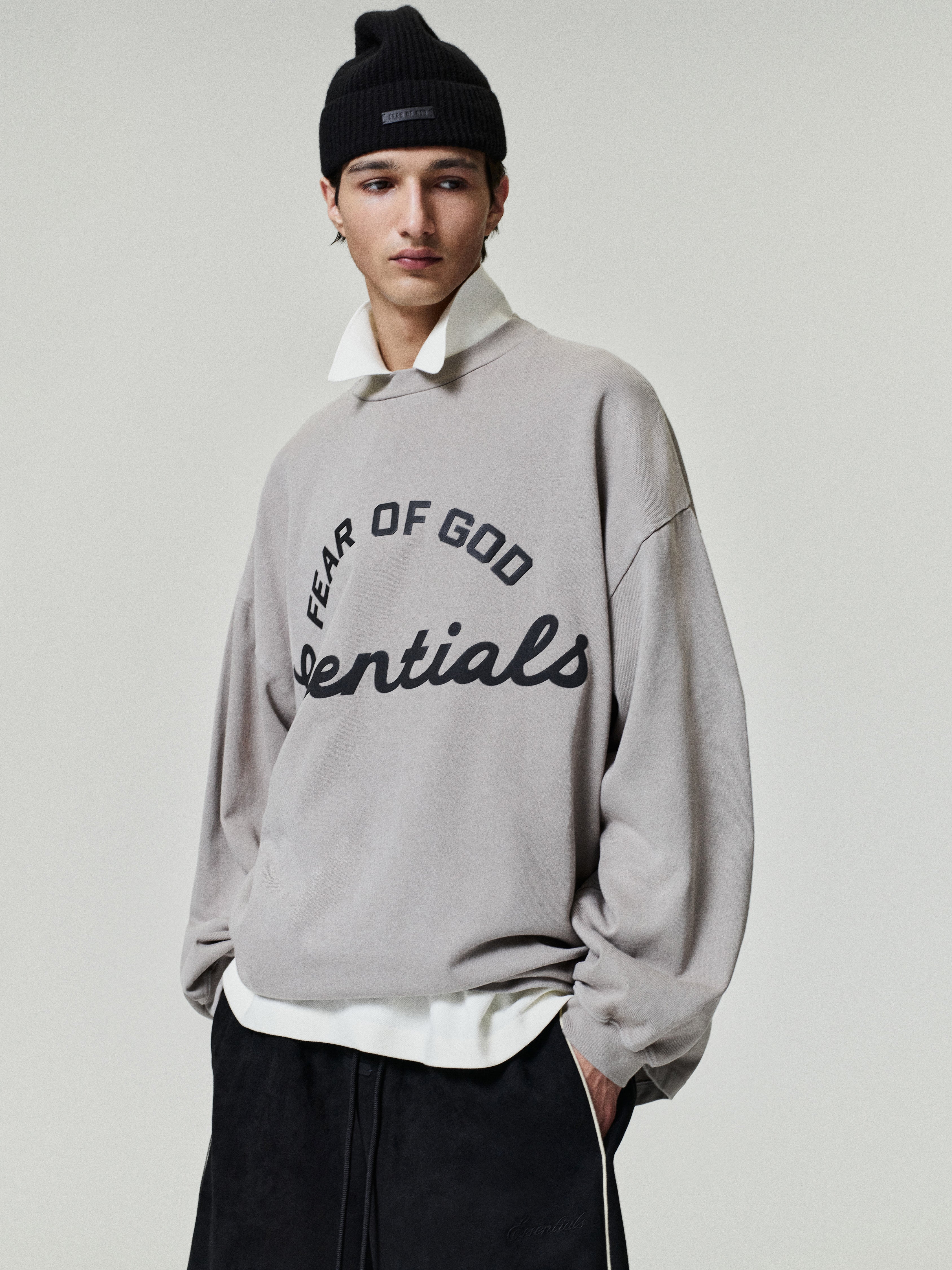 Person wearing a gray 'Fear of God Essentials' sweatshirt on a plain background