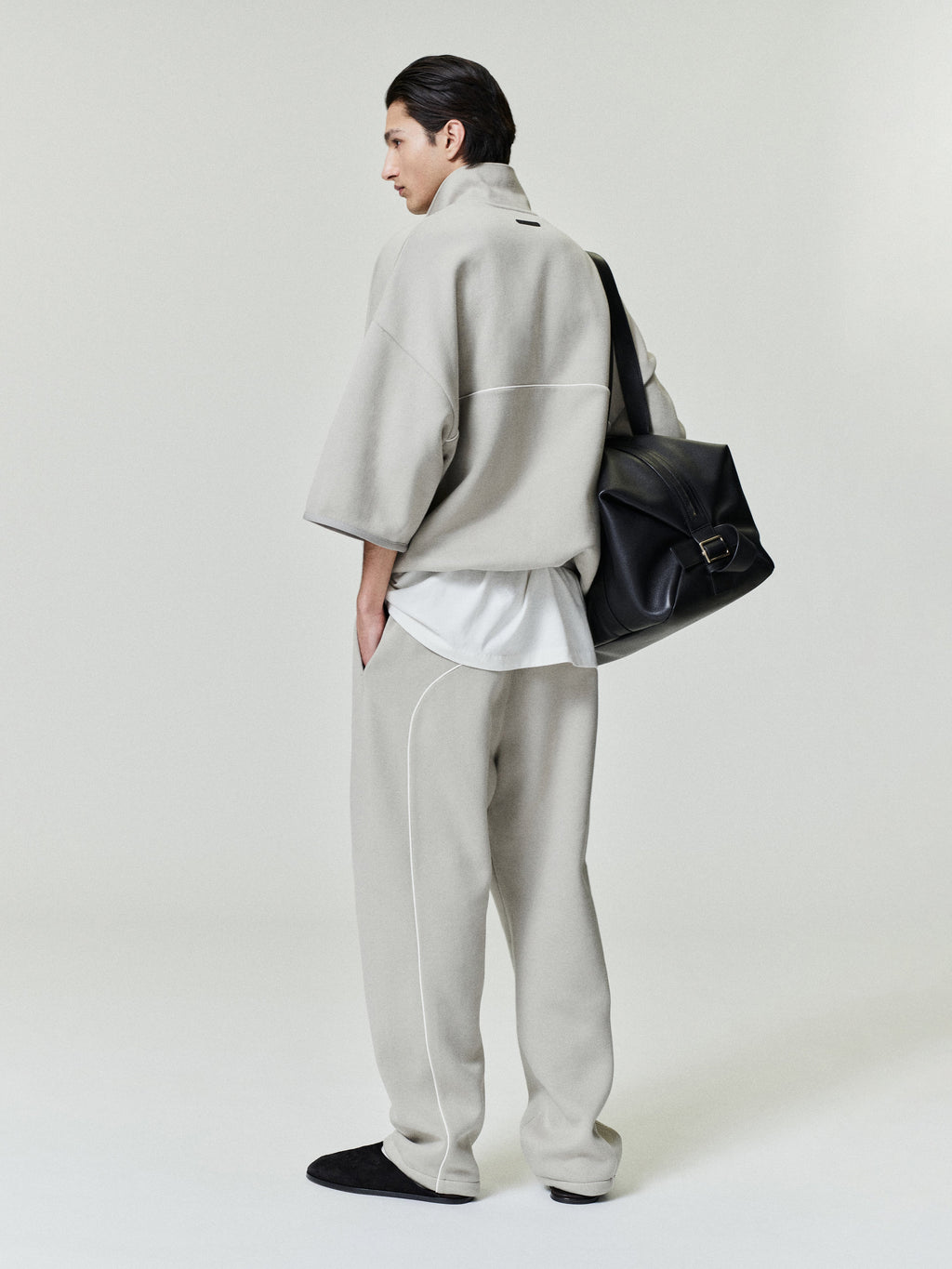 man wearing light beige cropped volume polo sweatshirt with 3/4 sleeves and matching relaxed fleece pants carrying black leather bag