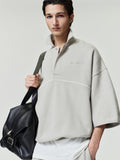 man wearing light beige cropped polo sweatshirt with 3/4 sleeves and subtle embroidered logo holding black leather bag