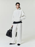 Person wearing a white hoodie and pants holding a black bag on a plain background