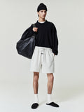 Person wearing a black sweater, white shorts, and black beanie holding a black bag on a plain background