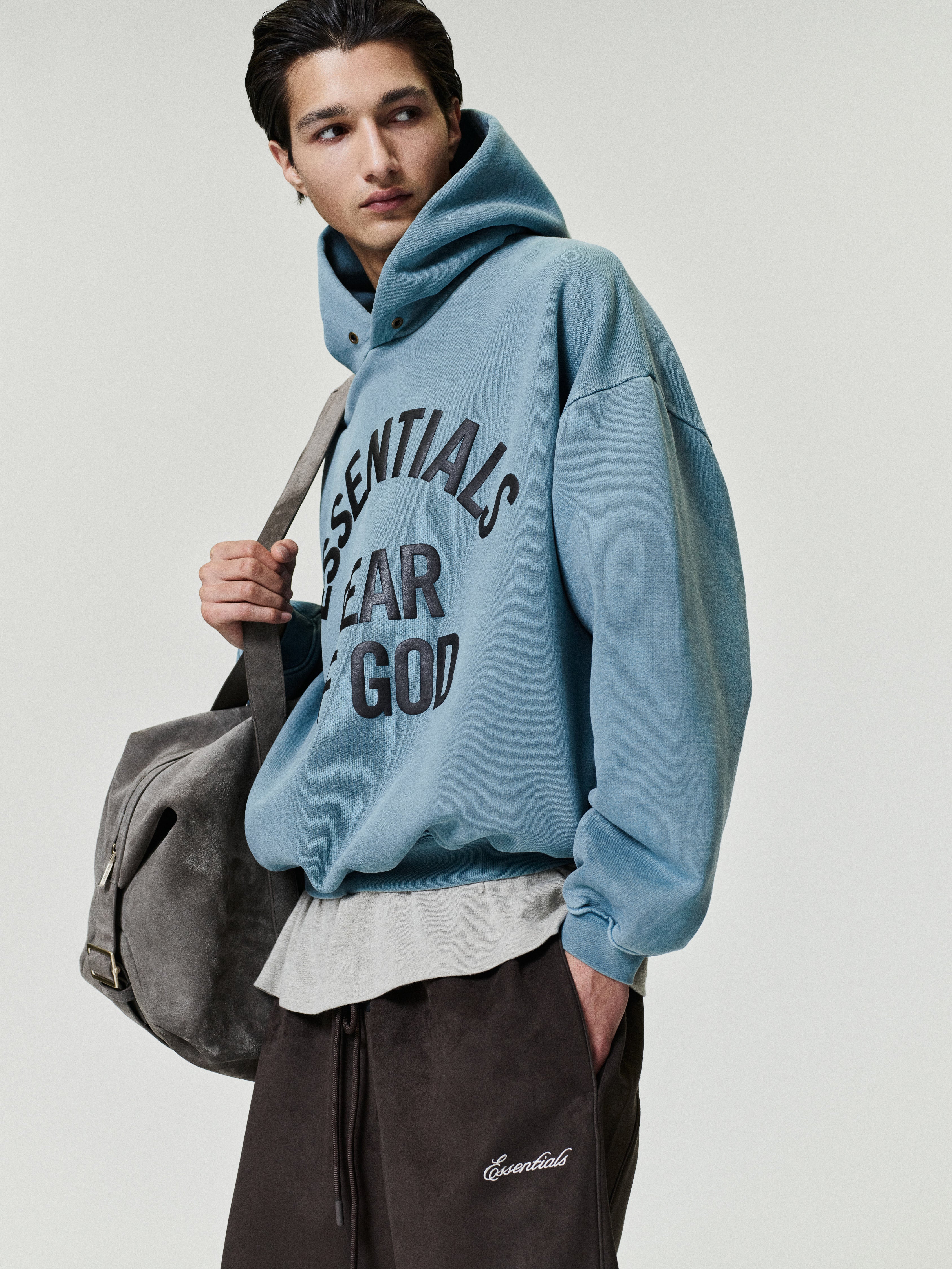 side view of cropped blue pigment-dyed heavyweight fleece hoodie with large black Essentials Fear of God print on chest