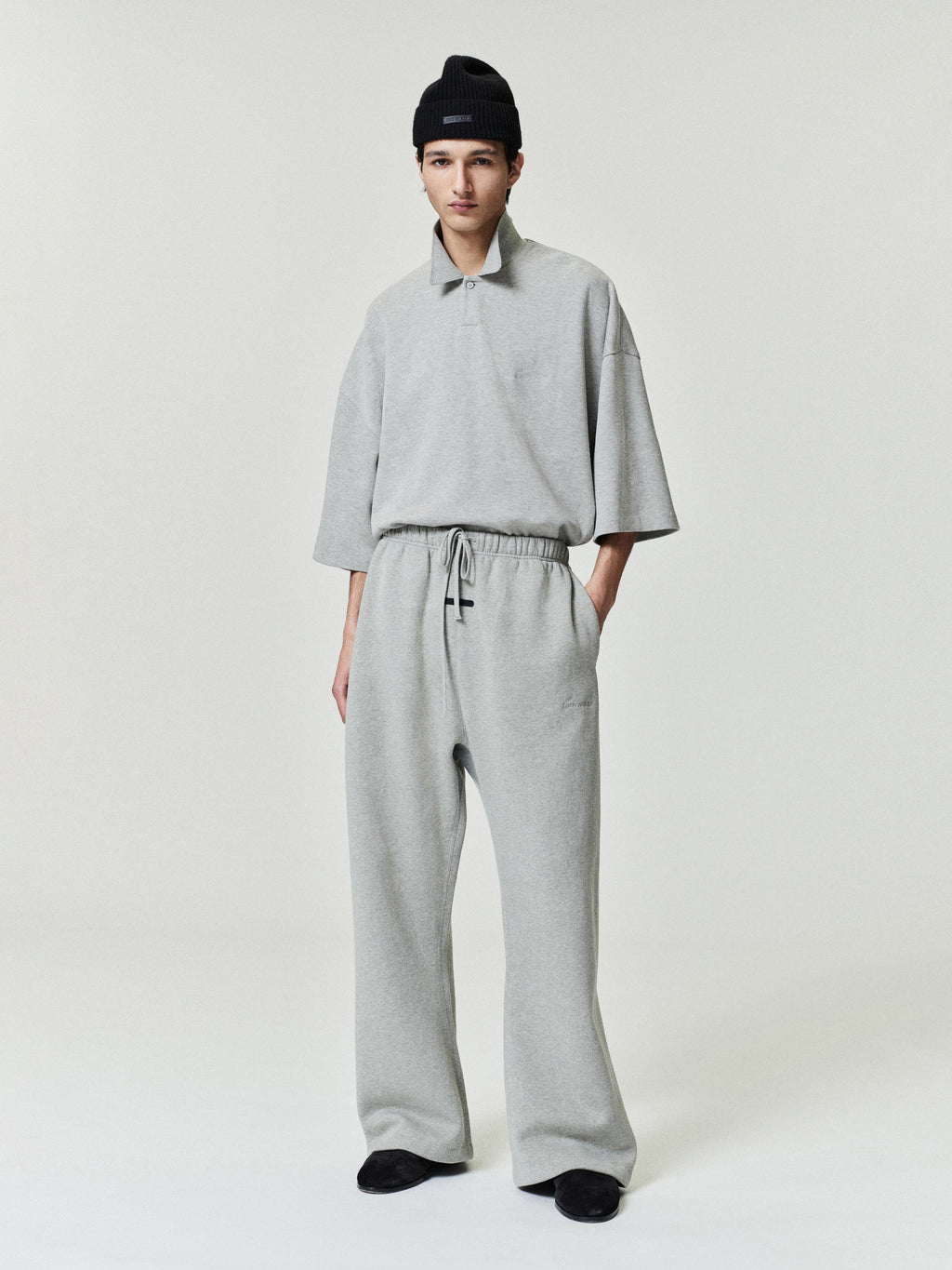 man in light grey relaxed fit sweatpants with elastic waistband and matching loose short sleeve top wearing black beanie