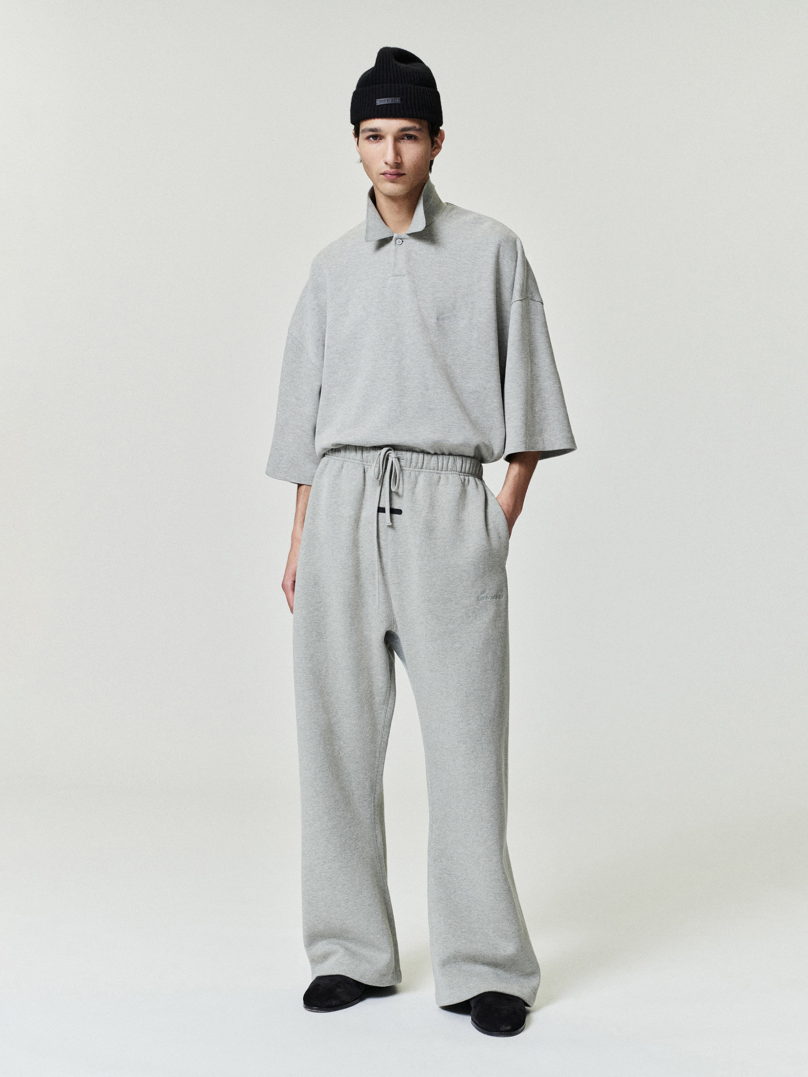 man in light grey relaxed fit sweatpants with elastic waistband and matching loose short sleeve top wearing black beanie