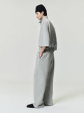 man wearing light grey relaxed fit flare sweatpants paired with matching oversized short sleeve top and black beanie