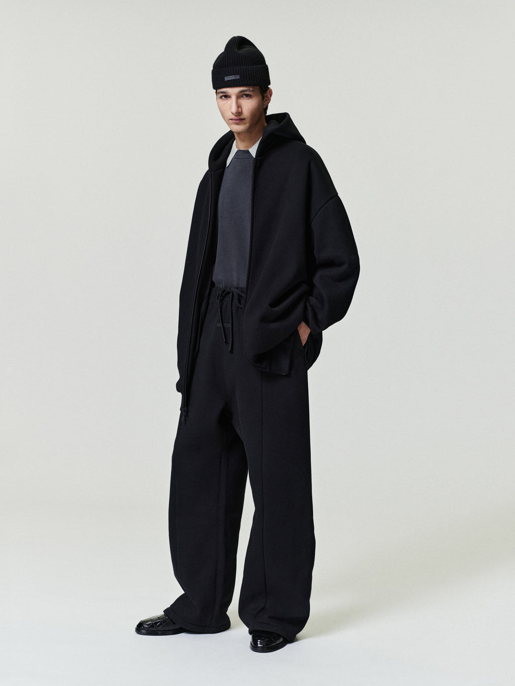 man wearing relaxed fit black canvas pleat front pants with elastic waistband and loose black jacket