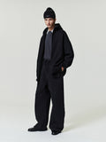 man wearing relaxed fit black canvas pleat front pants with elastic waistband and loose black jacket