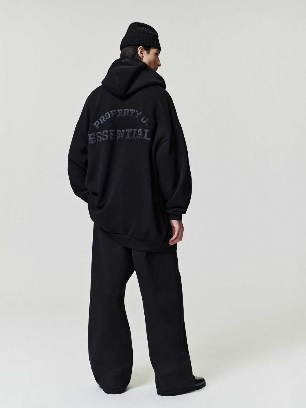 man in oversized black hoodie with graphic text paired with loose black pleated pants and black beanie