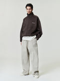 male model wearing dark brown bonded suede fleece oversized track jacket with subtle embroidered logo and beige wide-leg pants