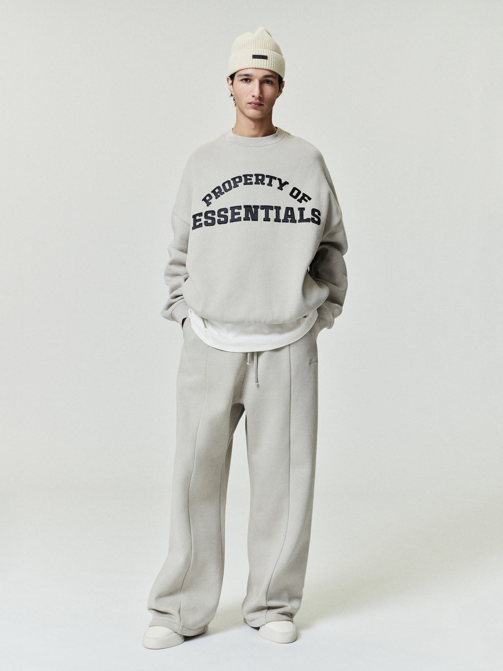 Person wearing a gray sweatshirt with 'PROPERTY OF ESSENTIALS' text on a white background