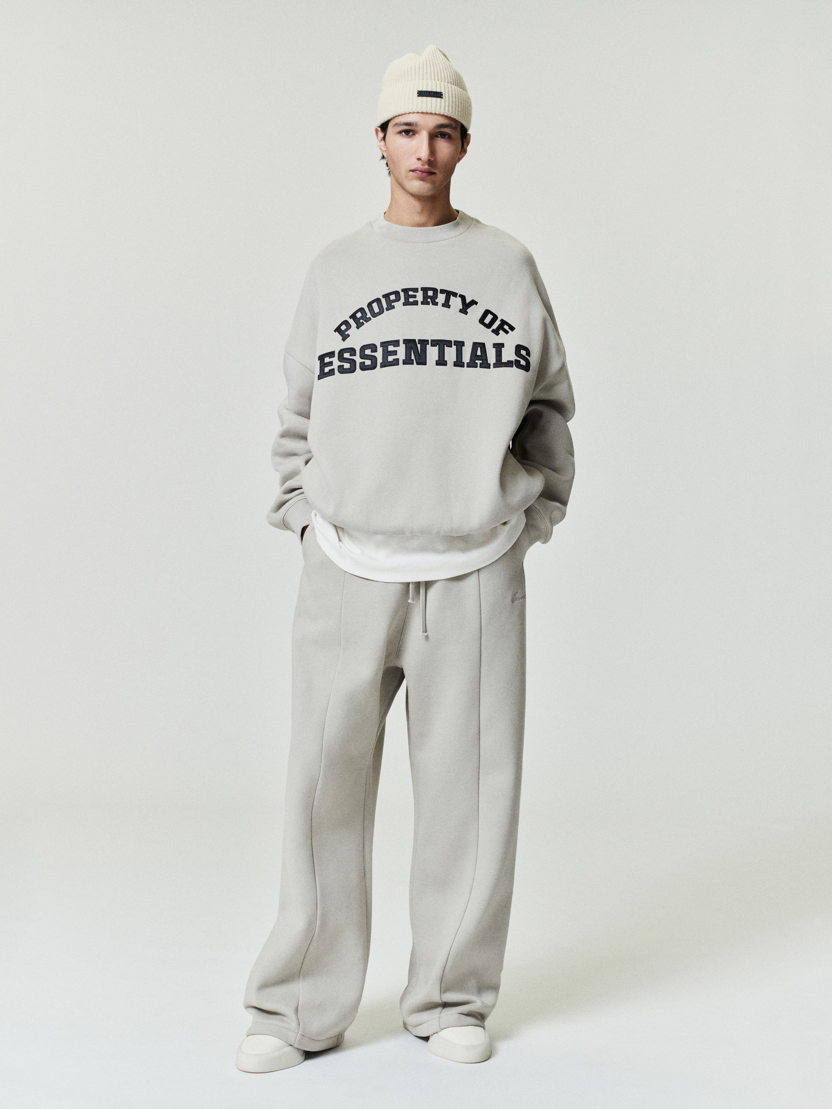 Person wearing a gray sweatshirt with 'PROPERTY OF ESSENTIALS' text on a white background