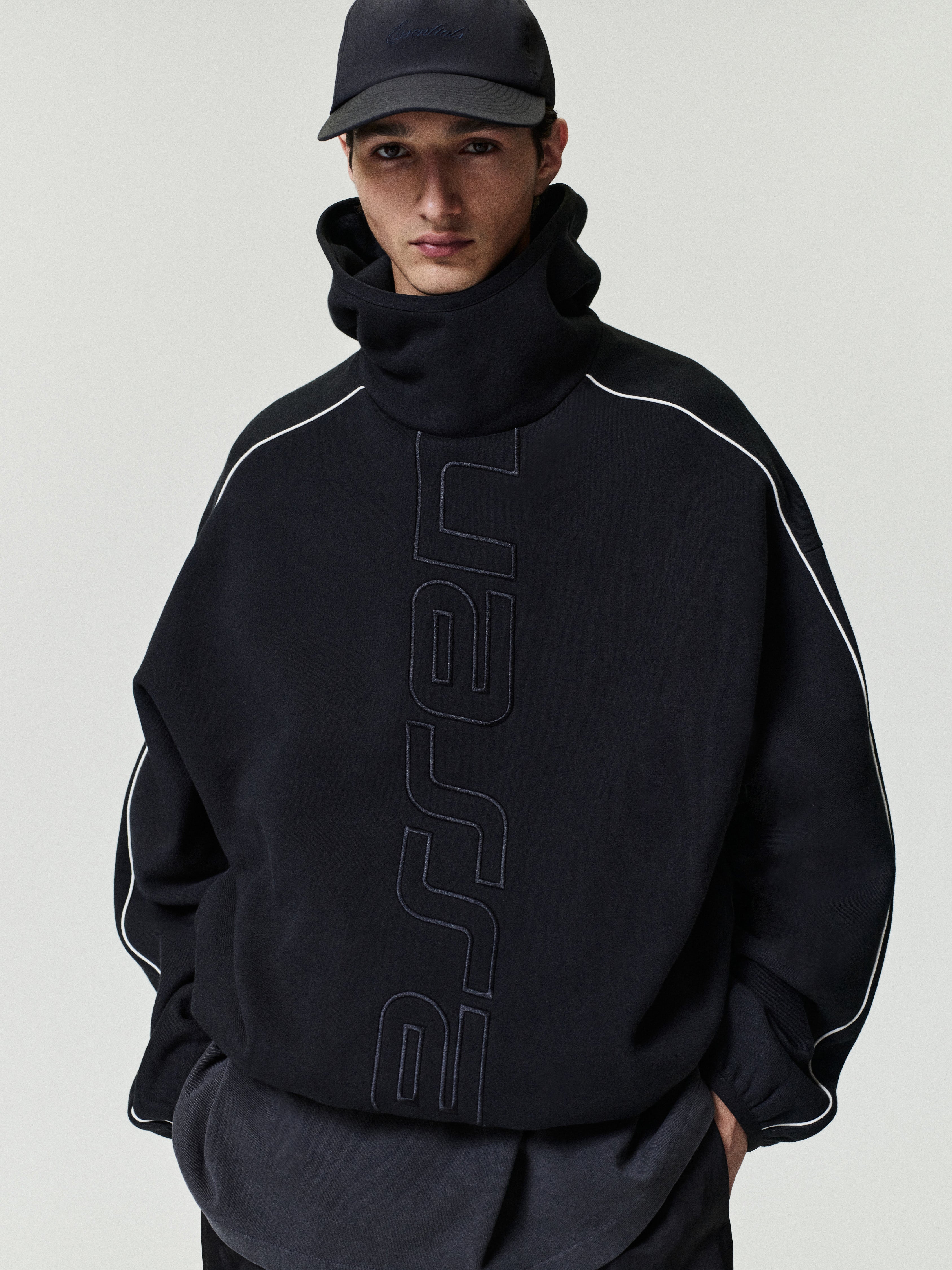 Person wearing a black hoodie with branding on a plain background