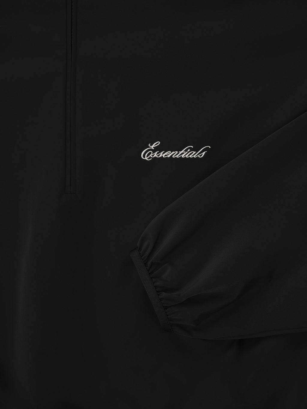 Close-up of black Sporty Nylon Half Zip focusing on sleeve cuff and white Essentials logo embroidery