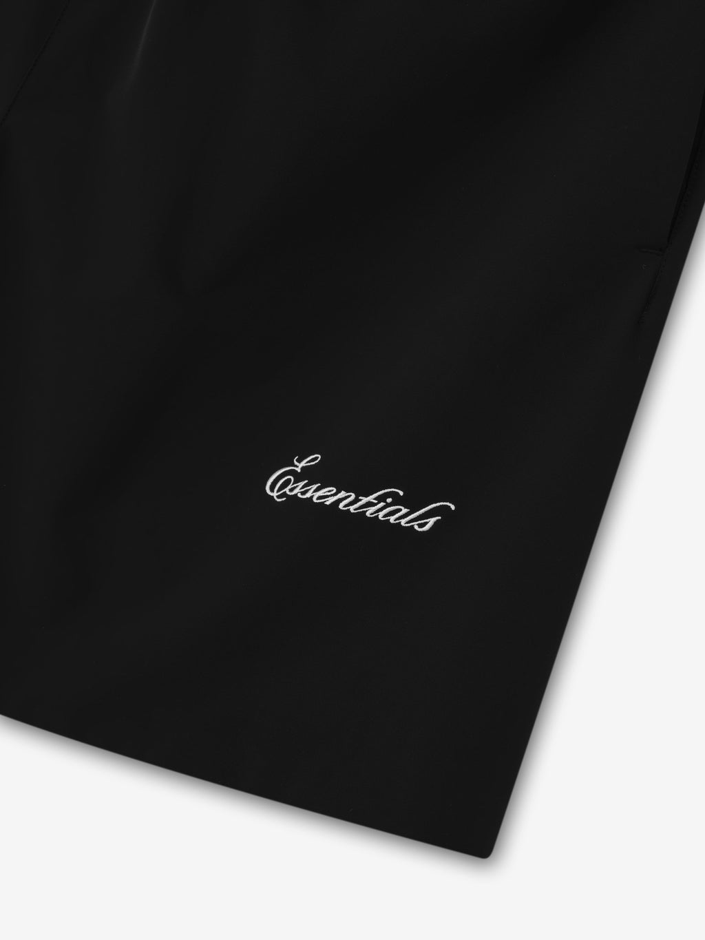 Close-up of black Sporty Nylon Classic Short fabric with white cursive Essentials logo embroidered near hem